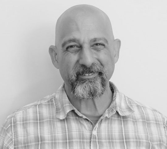 Black and white photo of a smiling, bald man with a salt and pepper mustache