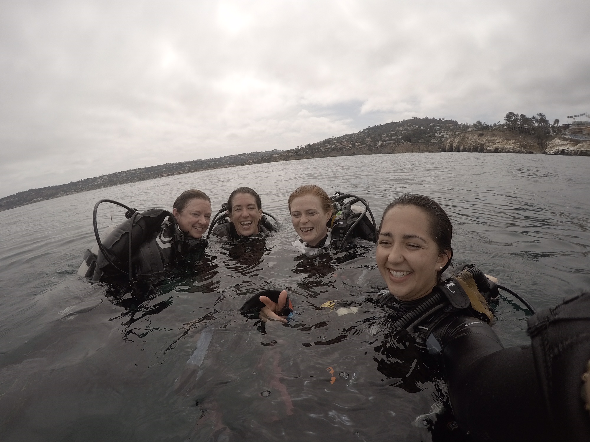 Four women in scuba gear, at the surface of the water smiling and laughing