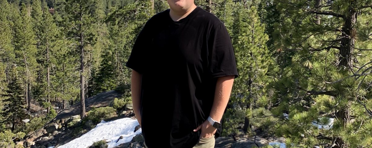 man in black shirt and green pants standing in front of a snowcapped mountain